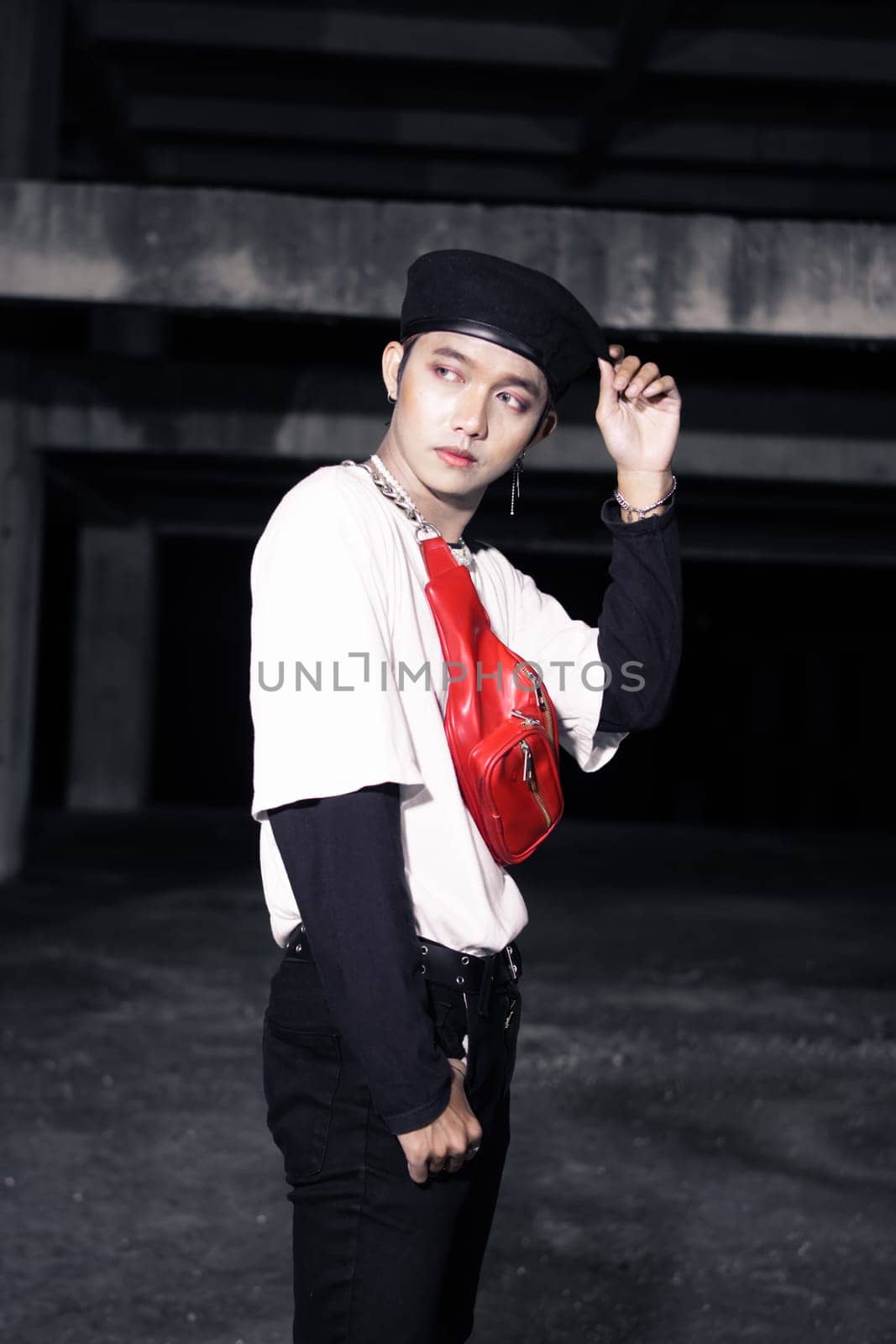 an Asian man in a white shirt wearing a red bag and a black hat in an old building at night
