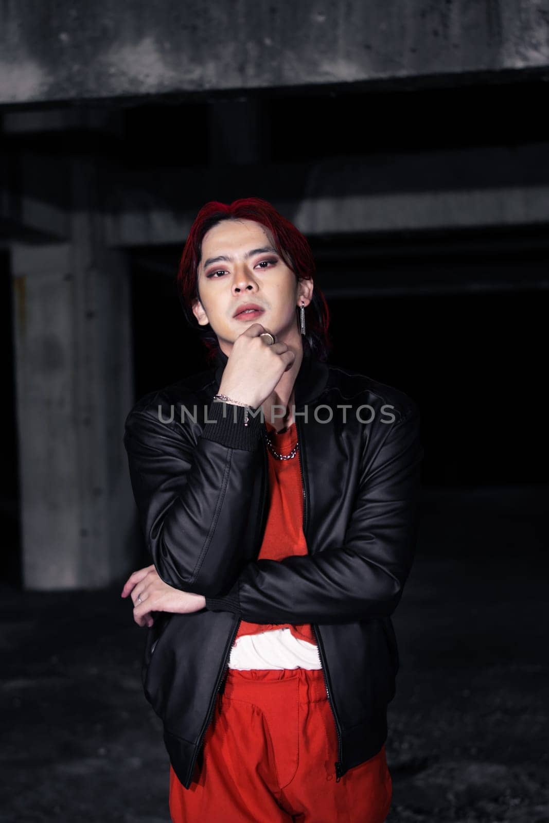 an asian man in a red shirt and black jacket posing with his hands in an abandoned warehouse