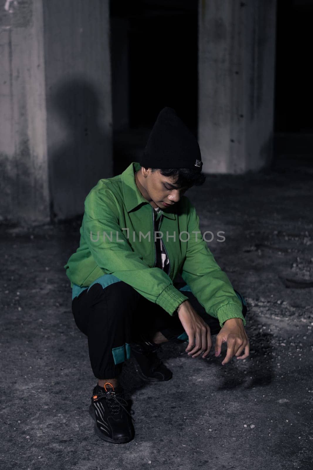 an Asian man squats while wearing a green jacket in a haunted building