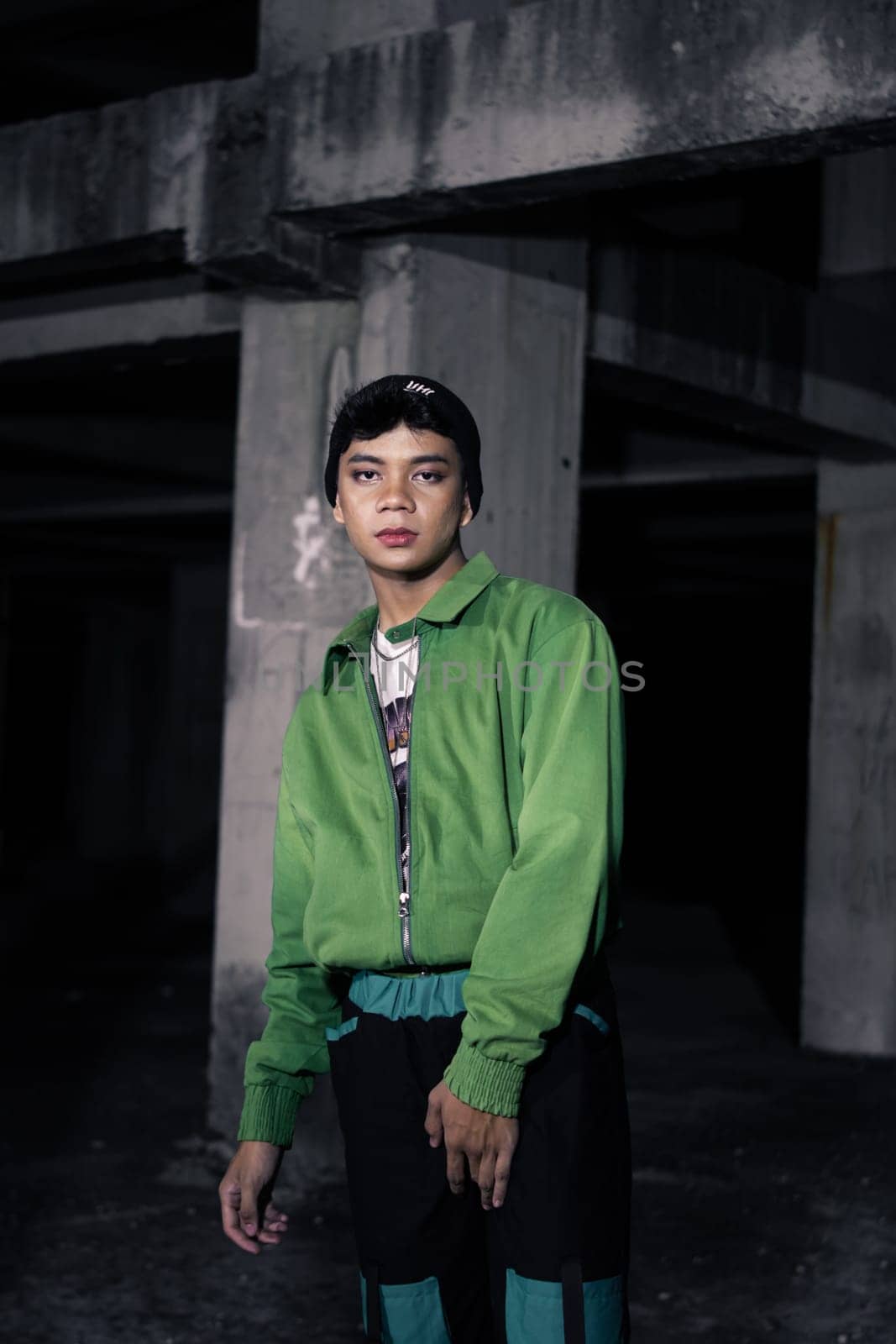 an Asian man smiles while wearing a green parachute jacket and black pants at night