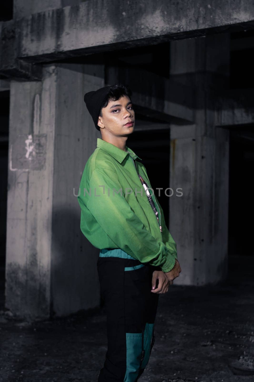 an Asian man smiles while wearing a green parachute jacket and black pants at night