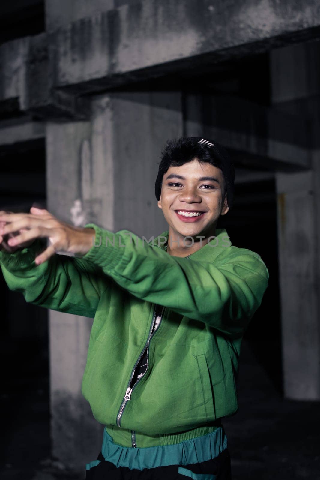 an Asian man smiles while wearing a green parachute jacket and black pants at night