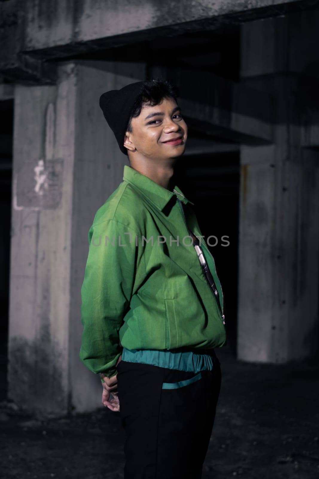 an Asian man smiles while wearing a green parachute jacket and black pants at night