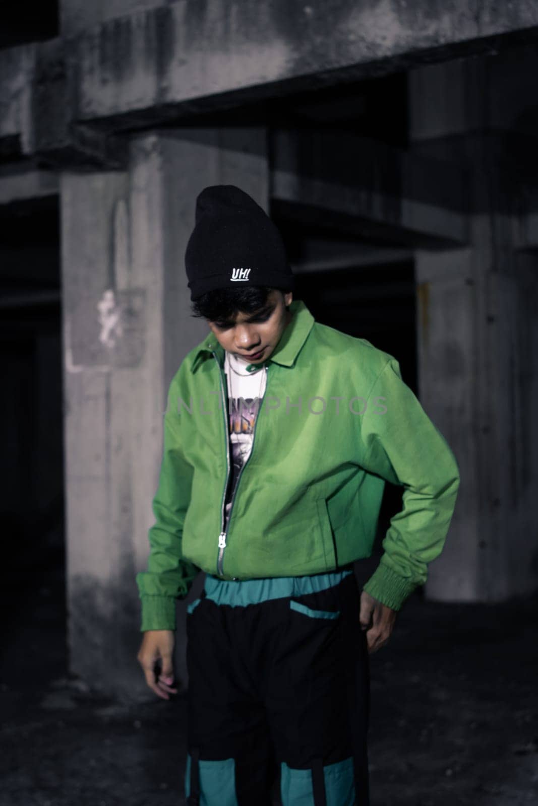 an Asian man smiles while wearing a green parachute jacket and black pants at night
