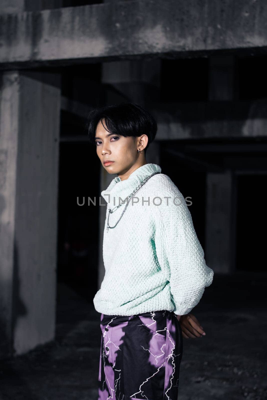 an asian man posing in a white sweater and a chain necklace around his neck in an old building