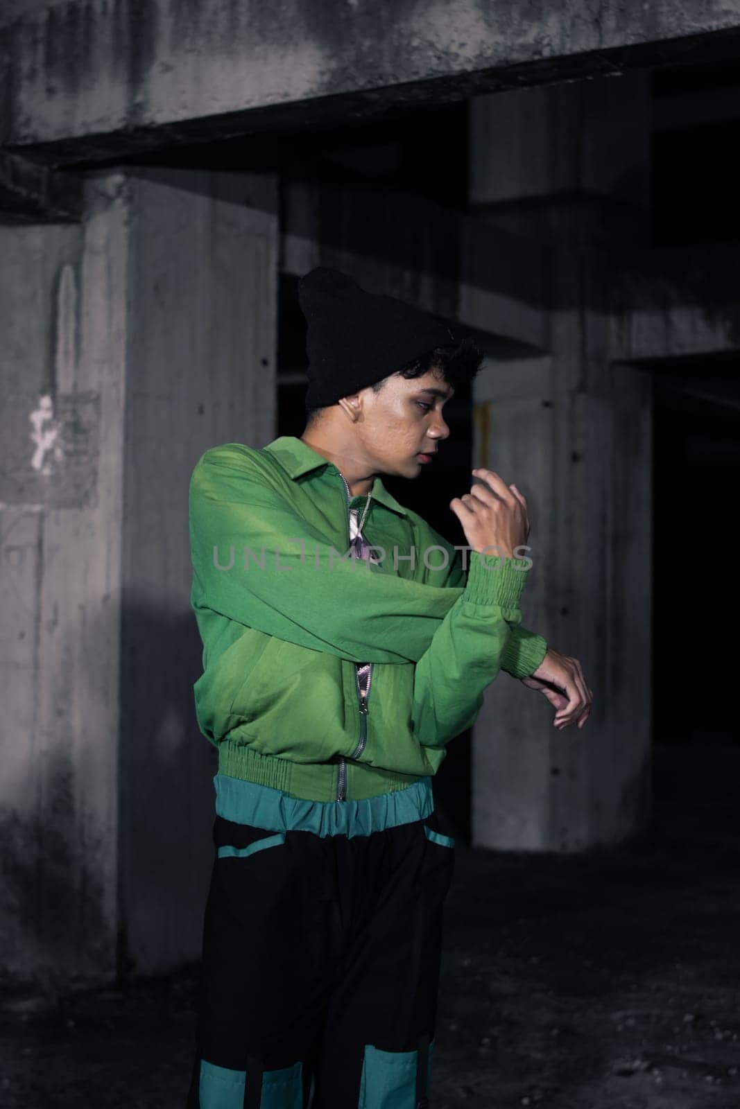 an Asian man smiles while wearing a green parachute jacket and black pants at night