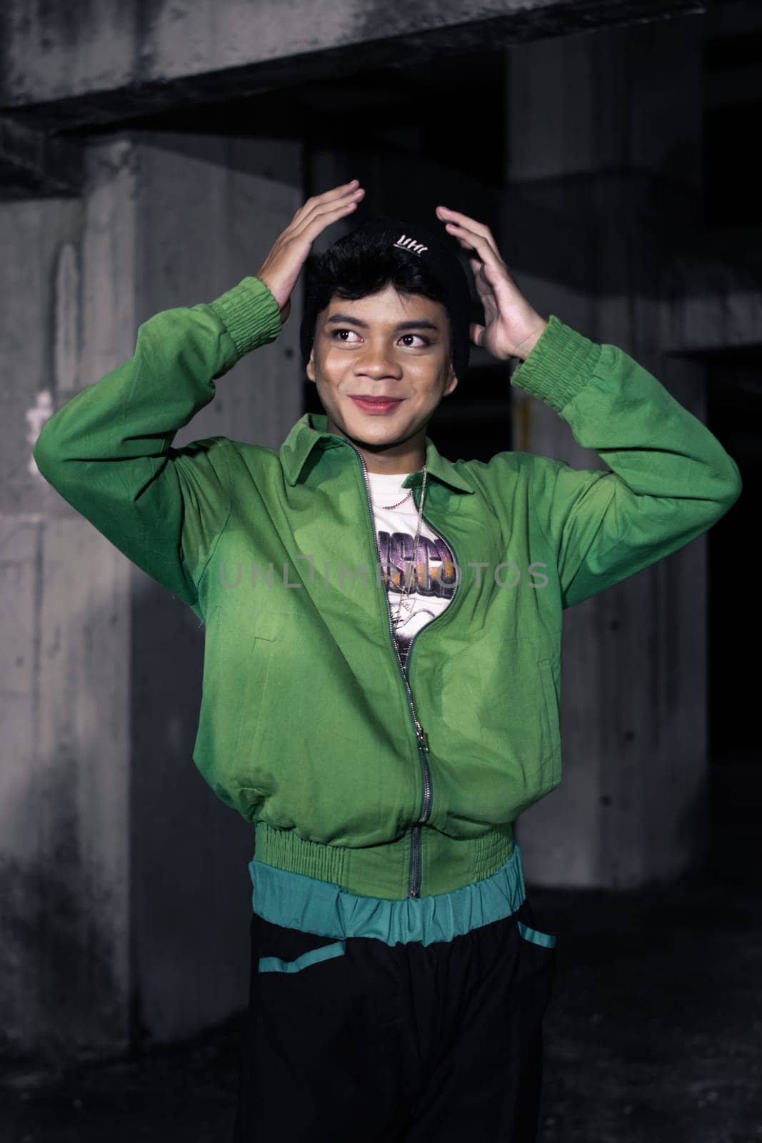 an Asian man smiles while wearing a green parachute jacket and black pants at night