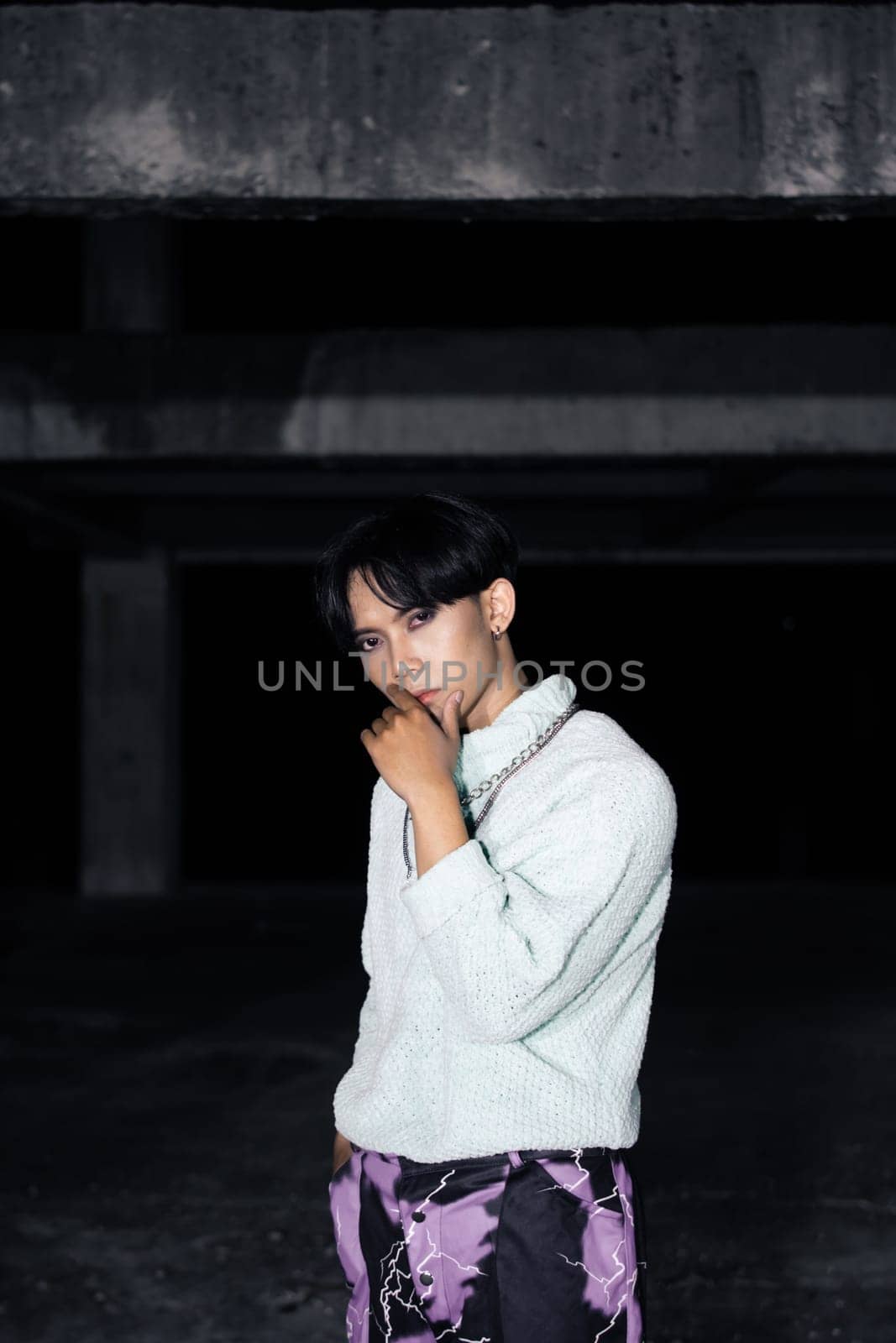 an asian man posing in a white sweater and a chain necklace around his neck in an old building
