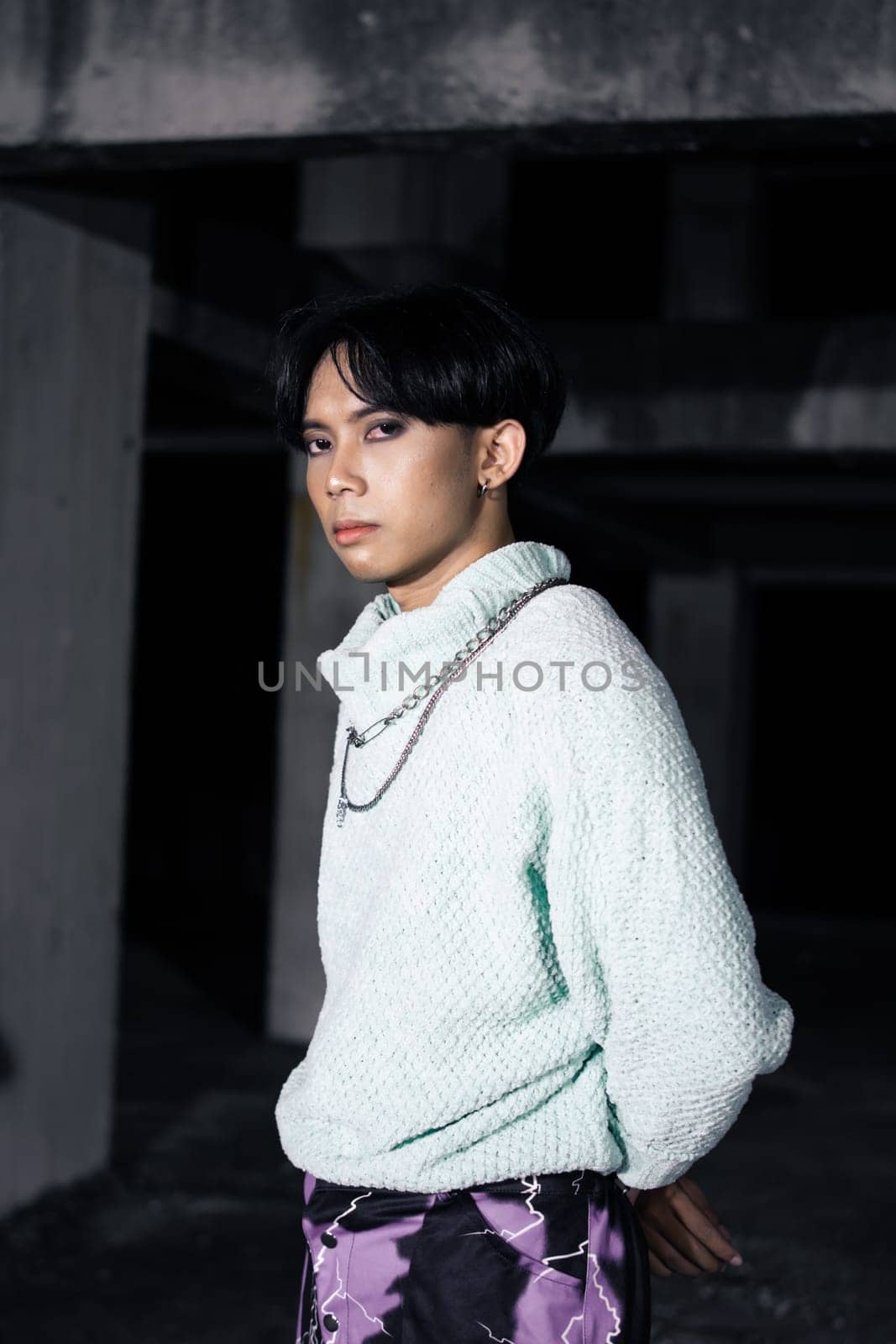 an asian man posing in a white sweater and a chain necklace around his neck in an old building