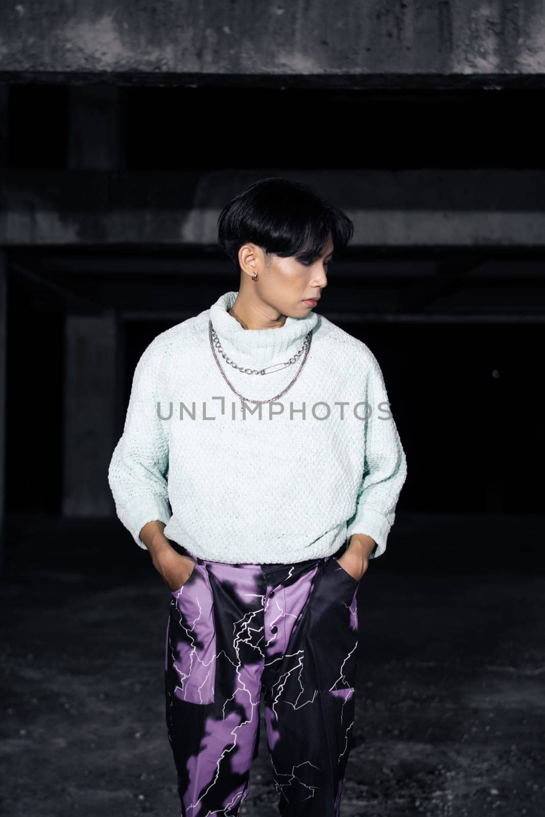 an asian man posing in a white sweater and a chain necklace around his neck in an old building