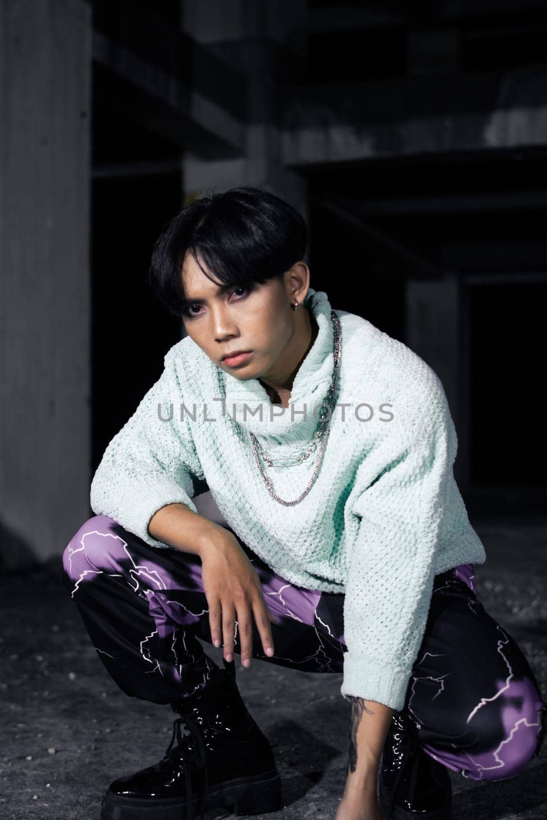 an asian man with black hair squats very masculine in an old building