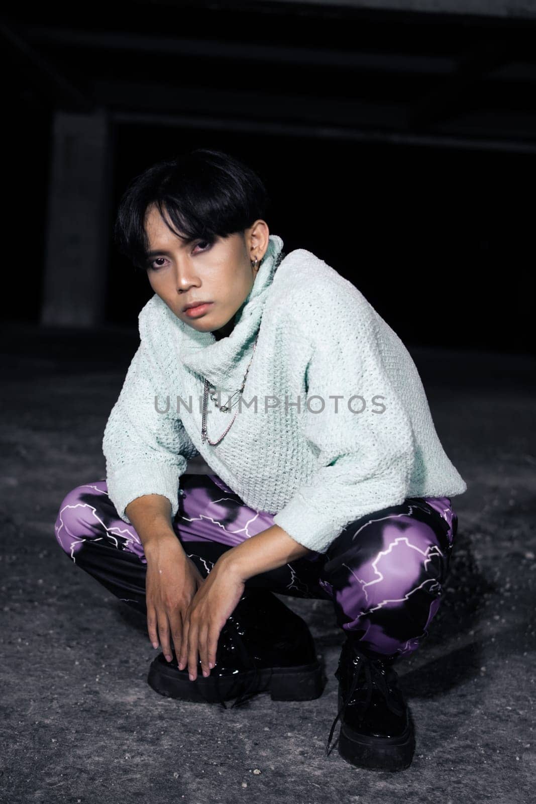 an asian man with black hair squats very masculine in an old building