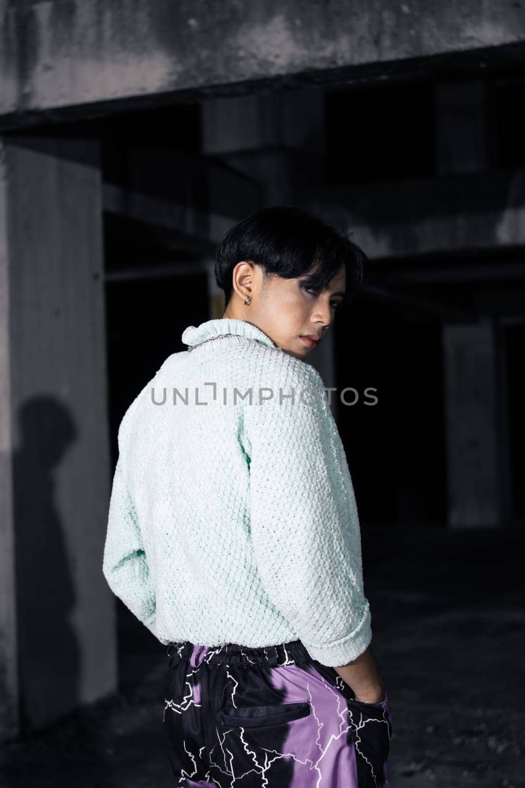 an asian man in black pants with a lightning pattern and a white sweater stands in a haunted building