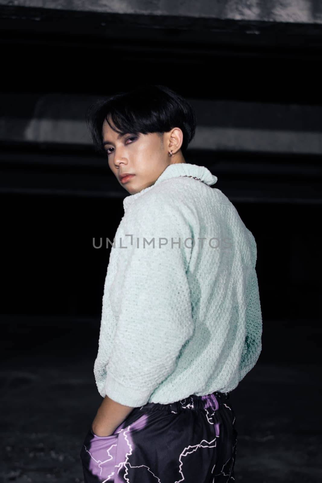 an asian man in black pants with a lightning pattern and a white sweater stands in a haunted building