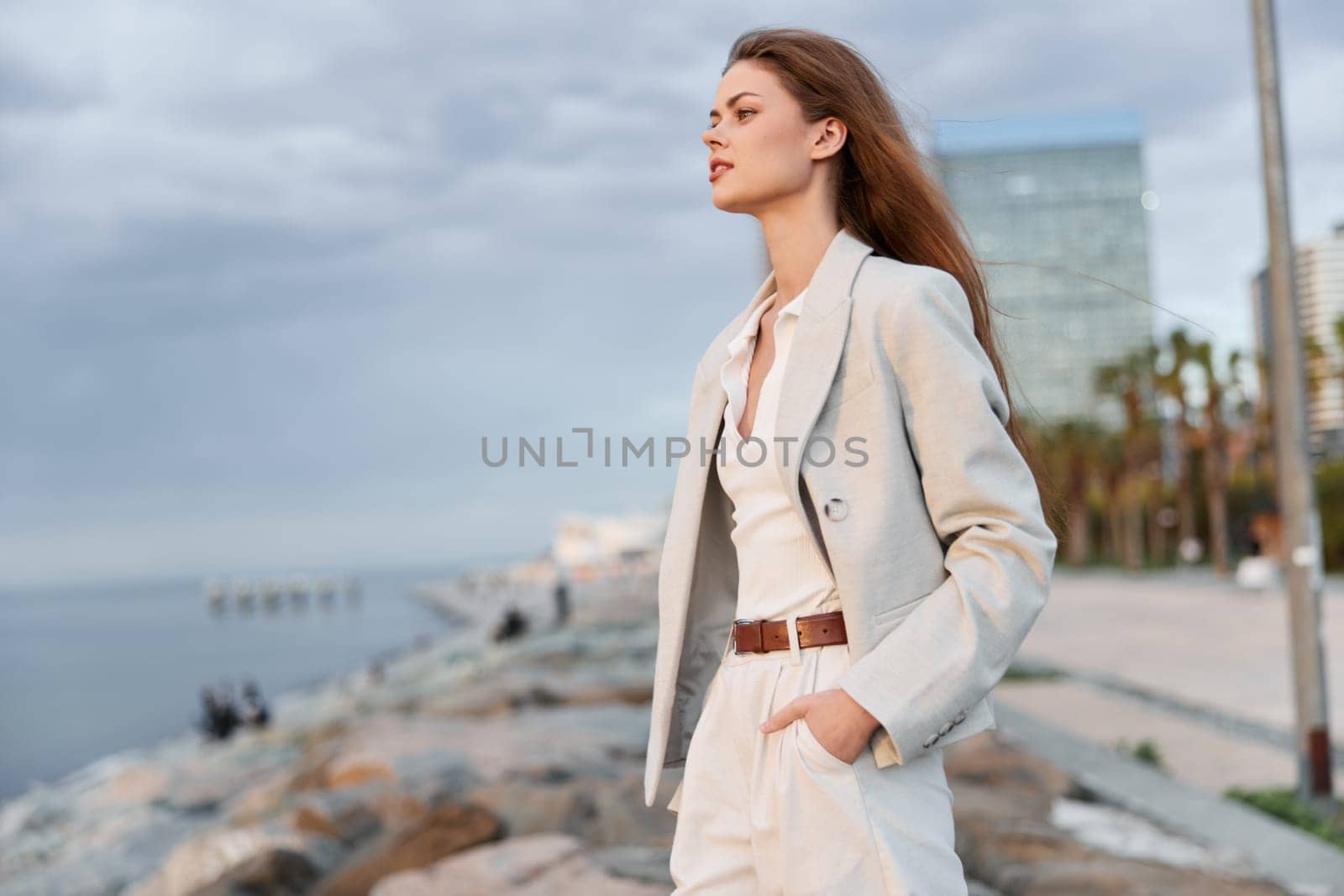 A poised woman in stylish business clothing stands by the waterfront, exuding confidence and professionalism. The serene background enhances the business concept.