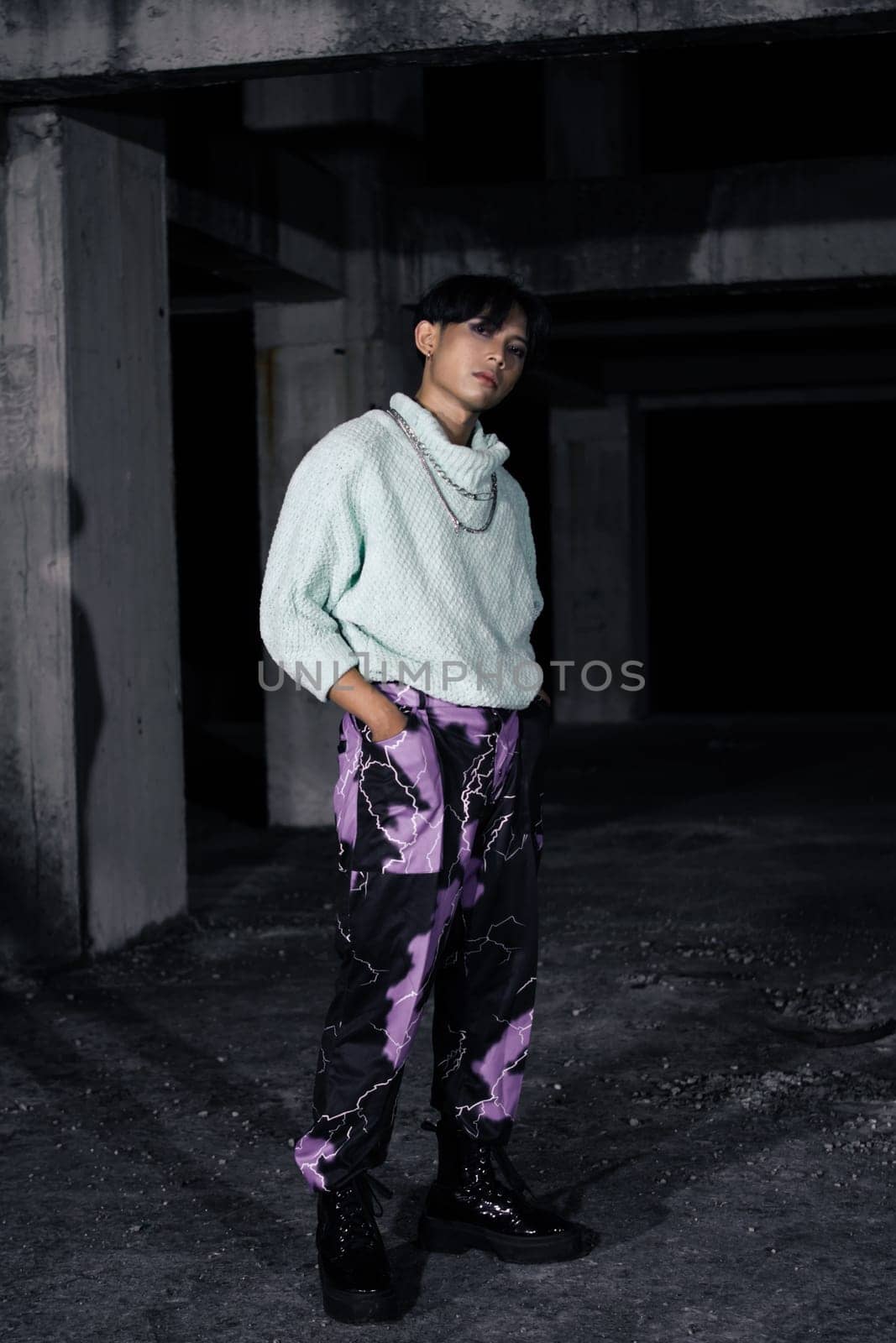 an asian man in black pants with a lightning pattern and a white sweater stands in a haunted building