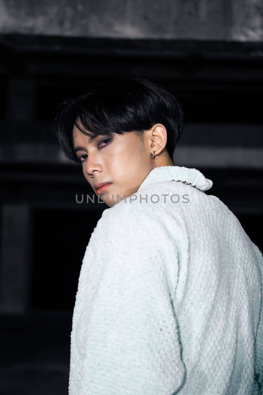 an asian man in black pants with a lightning pattern and a white sweater stands in a haunted building