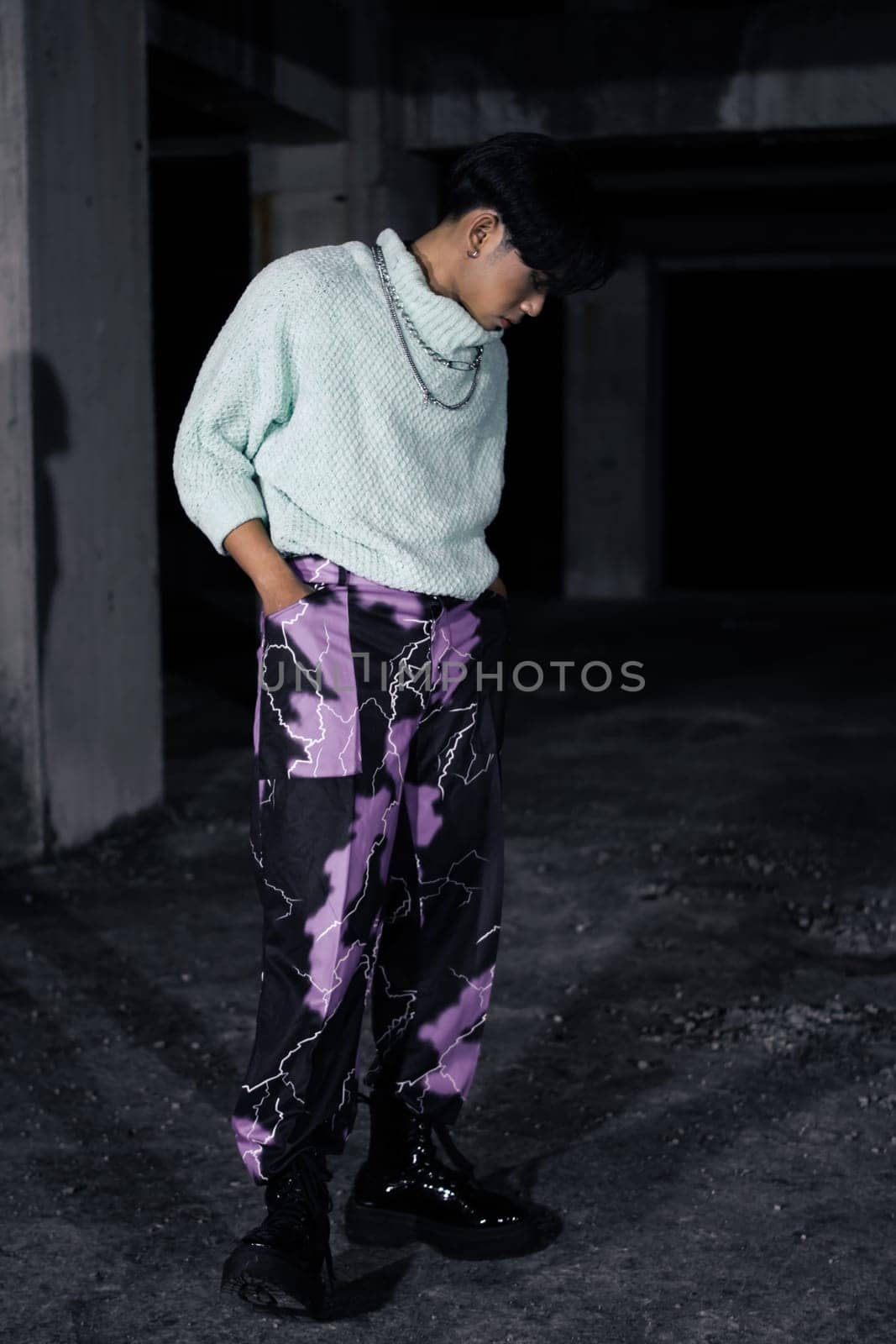 an asian man in black pants with a lightning pattern and a white sweater stands in a haunted building
