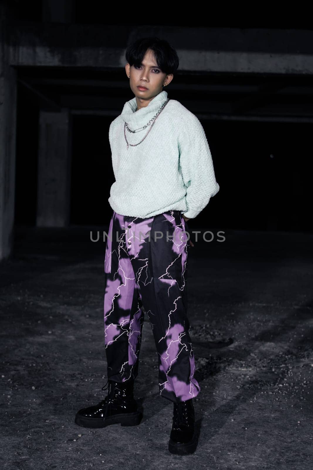 an asian man in black pants with a lightning pattern and a white sweater stands in a haunted building