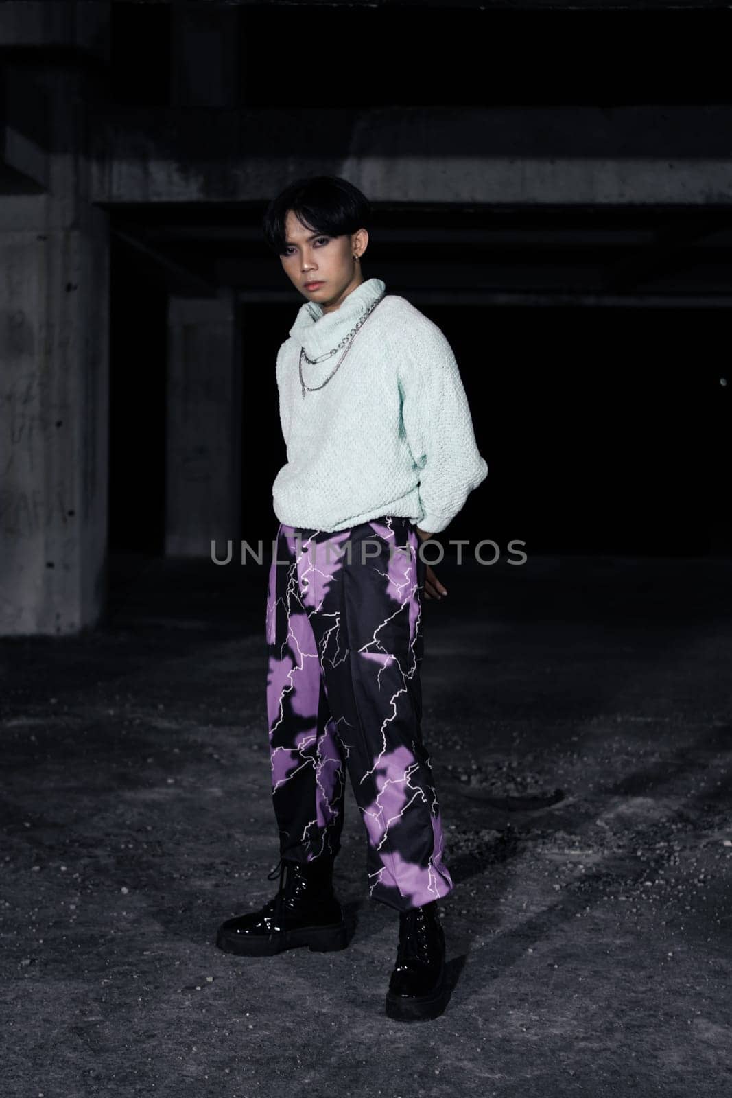 an asian man in black pants with a lightning pattern and a white sweater stands in a haunted building