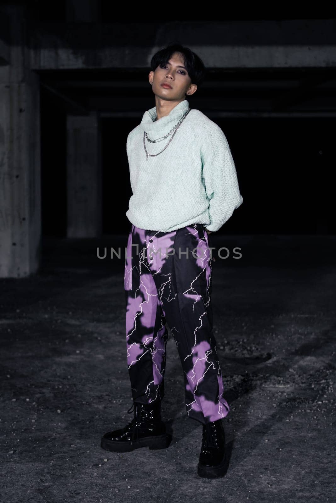 an asian man in black pants with a lightning pattern and a white sweater stands in a haunted building