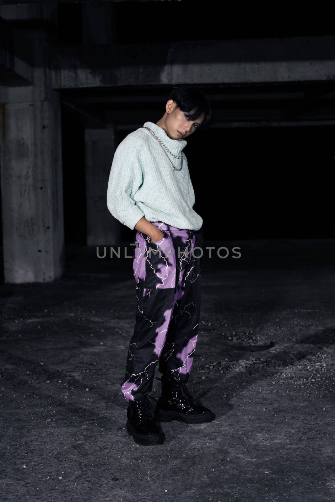 an asian man in black pants with a lightning pattern and a white sweater stands in a haunted building