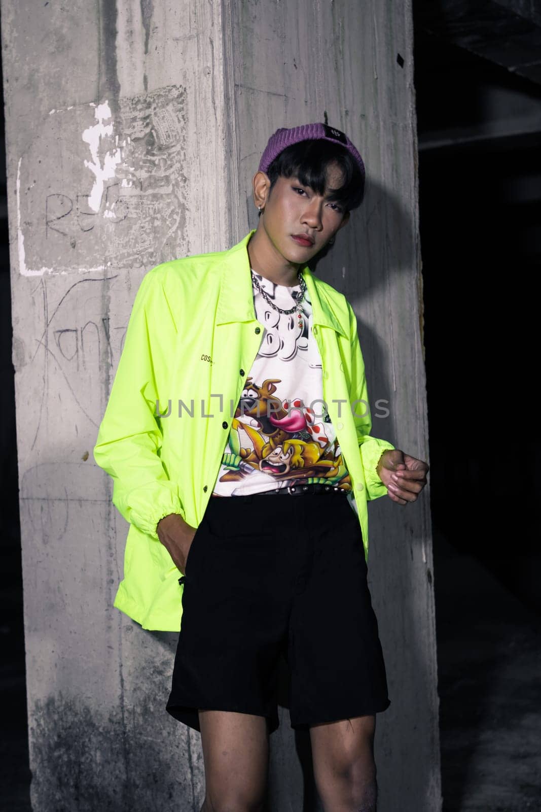 an asian man in a lime colored jacket leaning against a disused building pillar looking very handsome at night