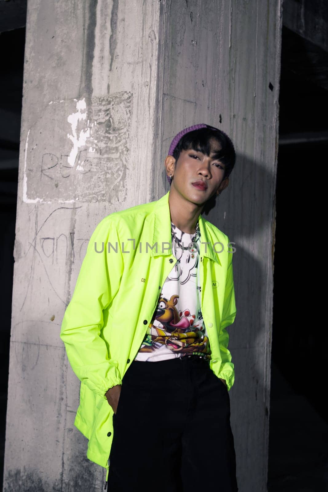 an asian man in a lime colored jacket leaning against a disused building pillar looking very handsome at night