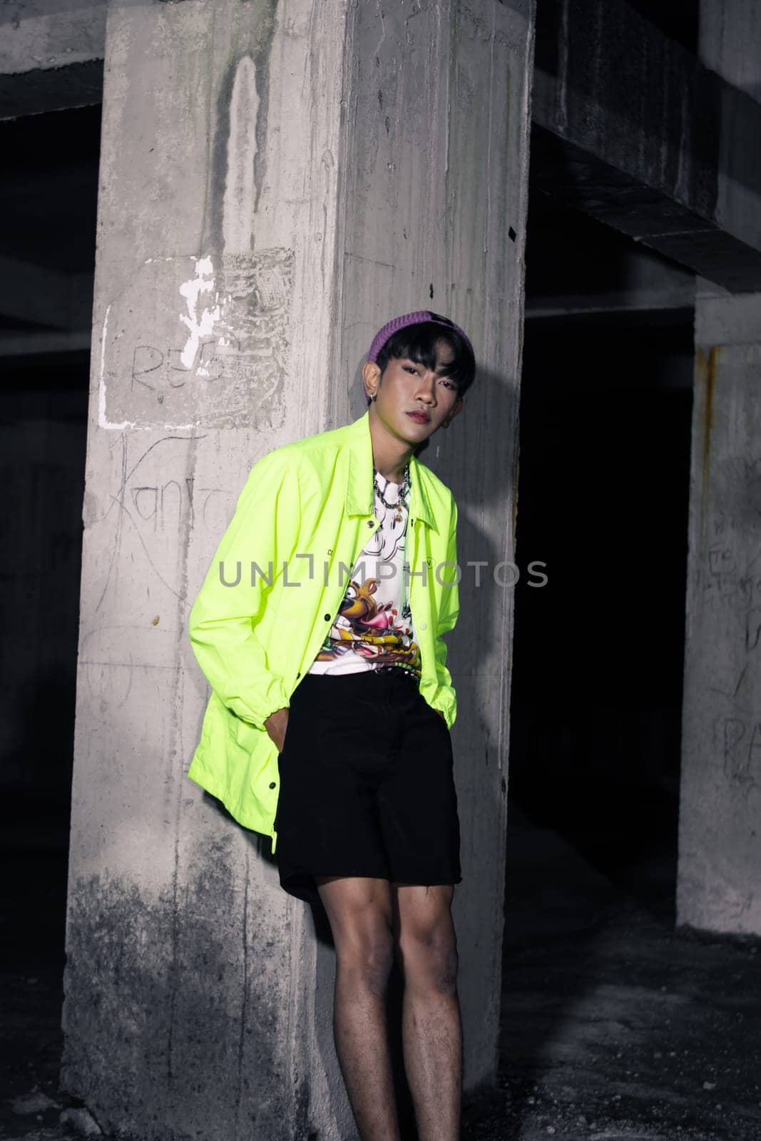 an asian man in a lime colored jacket leaning against a disused building pillar looking very handsome at night