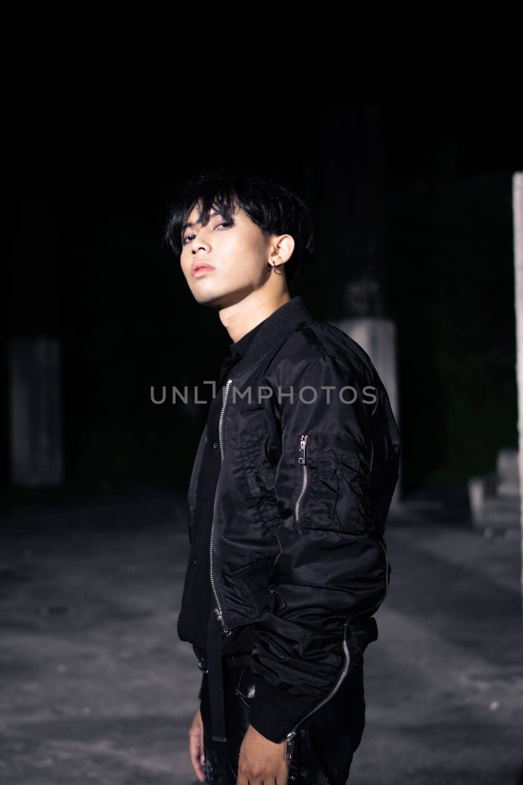 an asian man in a black parachute jacket posing very manly in a building at night