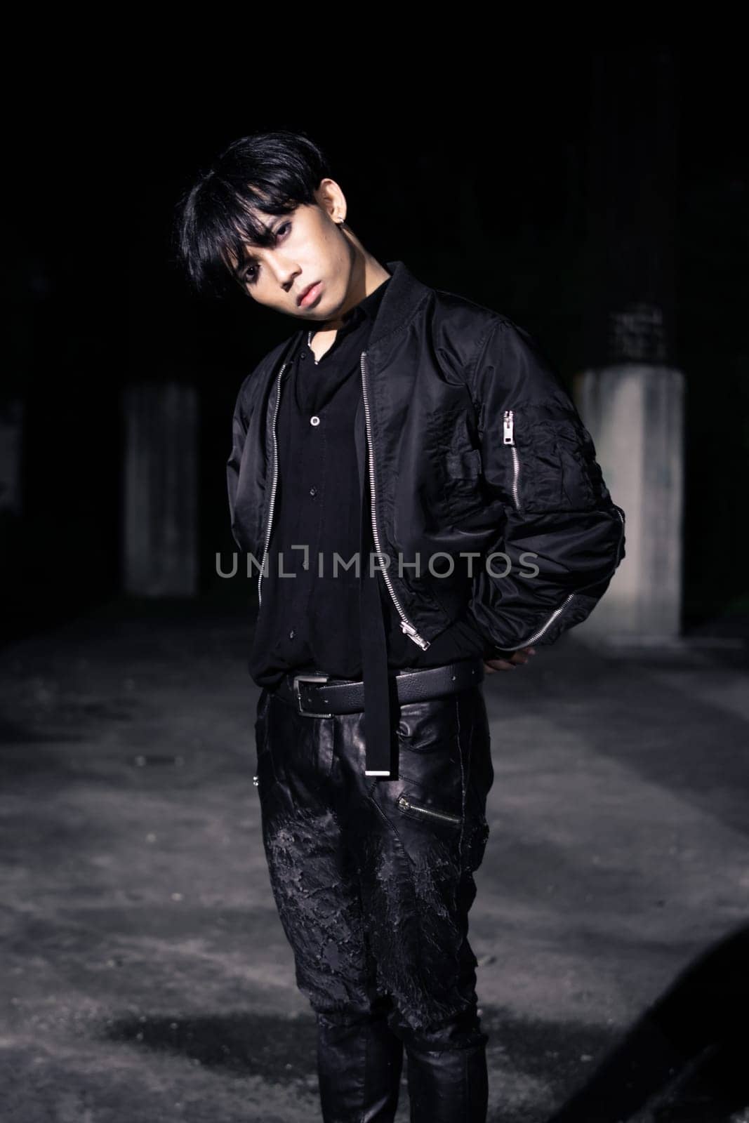 an asian man in a black parachute jacket posing very manly in a building at night