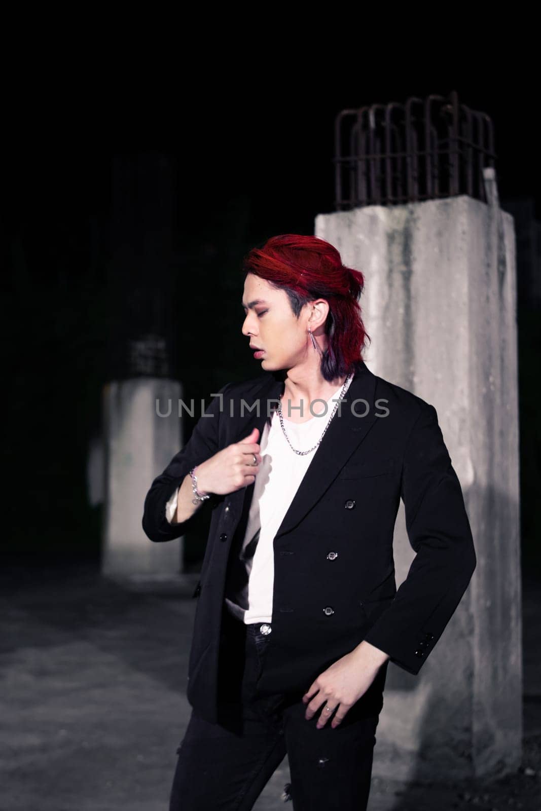 a red haired asian man wearing a white t shirt and black suit in an old building at night