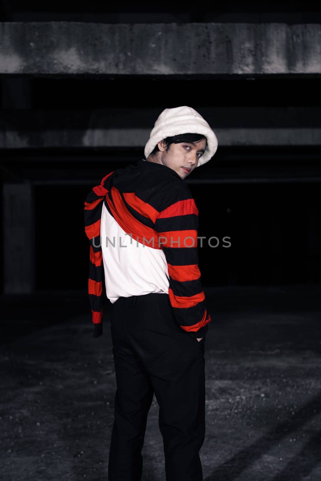 an Asian man with a striped red shirt and a chain necklace around his neck in an old building