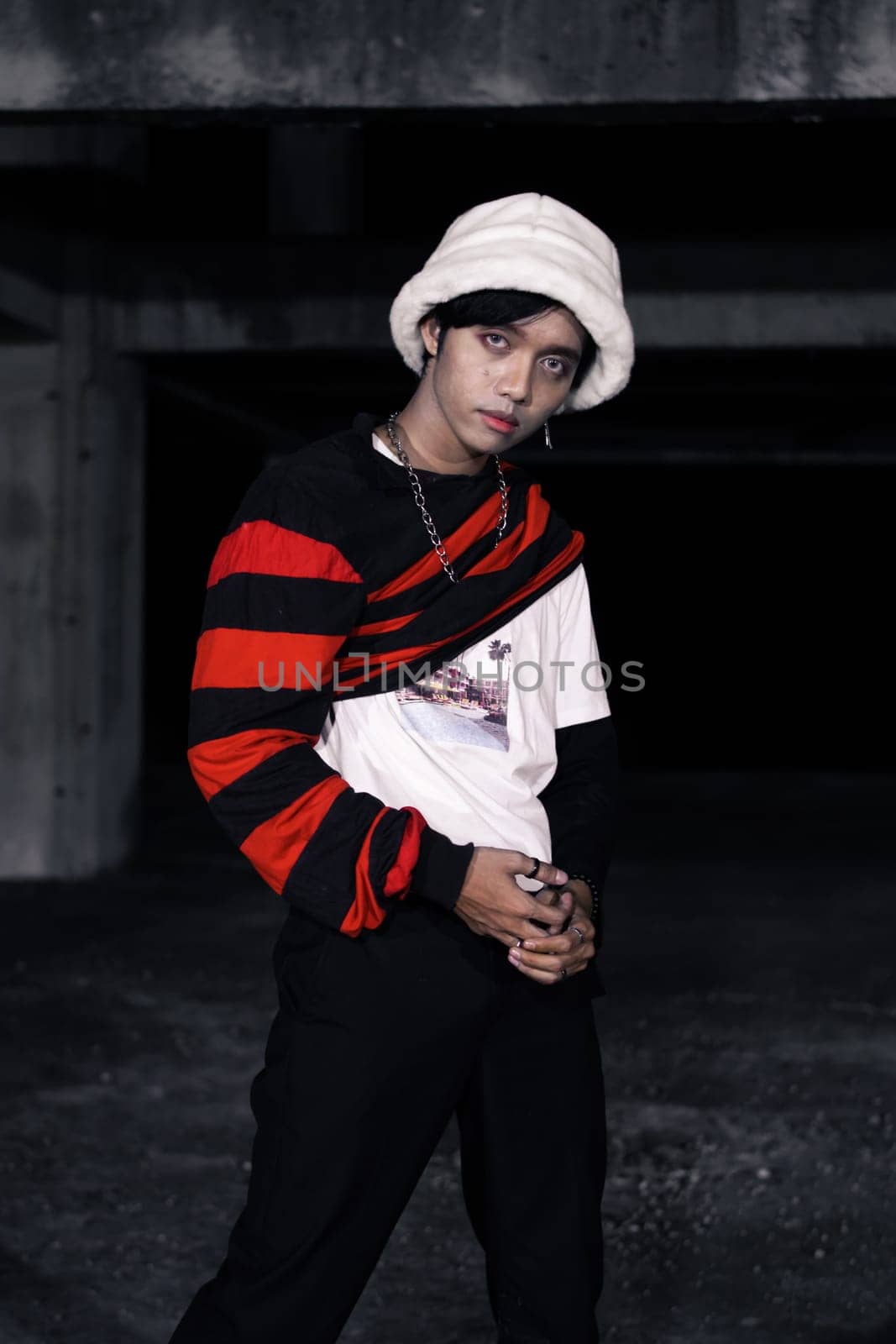 an Asian man with a striped red shirt and a chain necklace around his neck in an old building