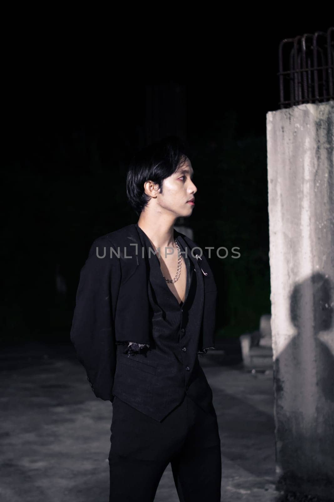 an Asian man is standing in black clothes and wearing makeup at night