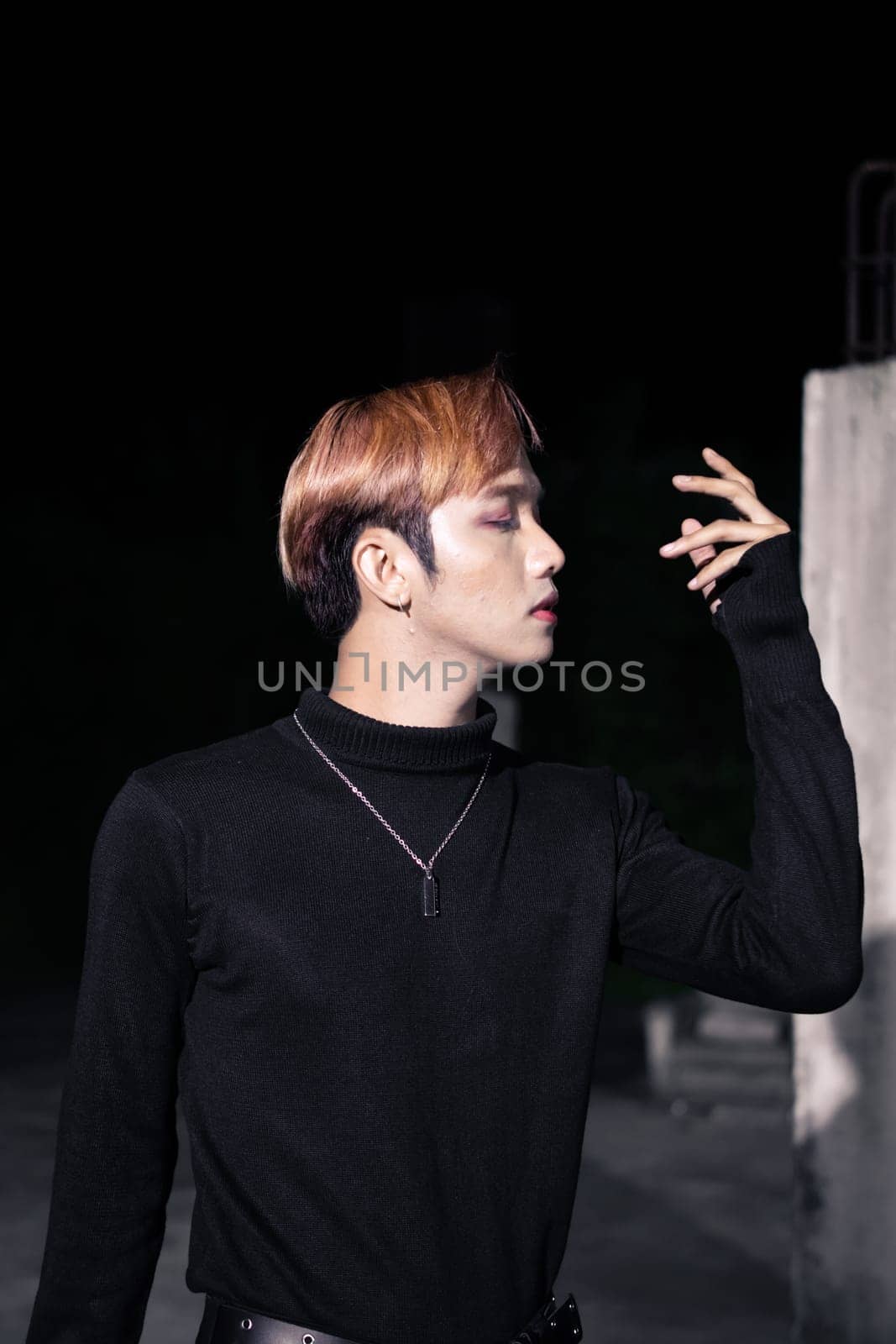 portrait of a blonde Asian man in a black sweater and black belt around his waist posing
