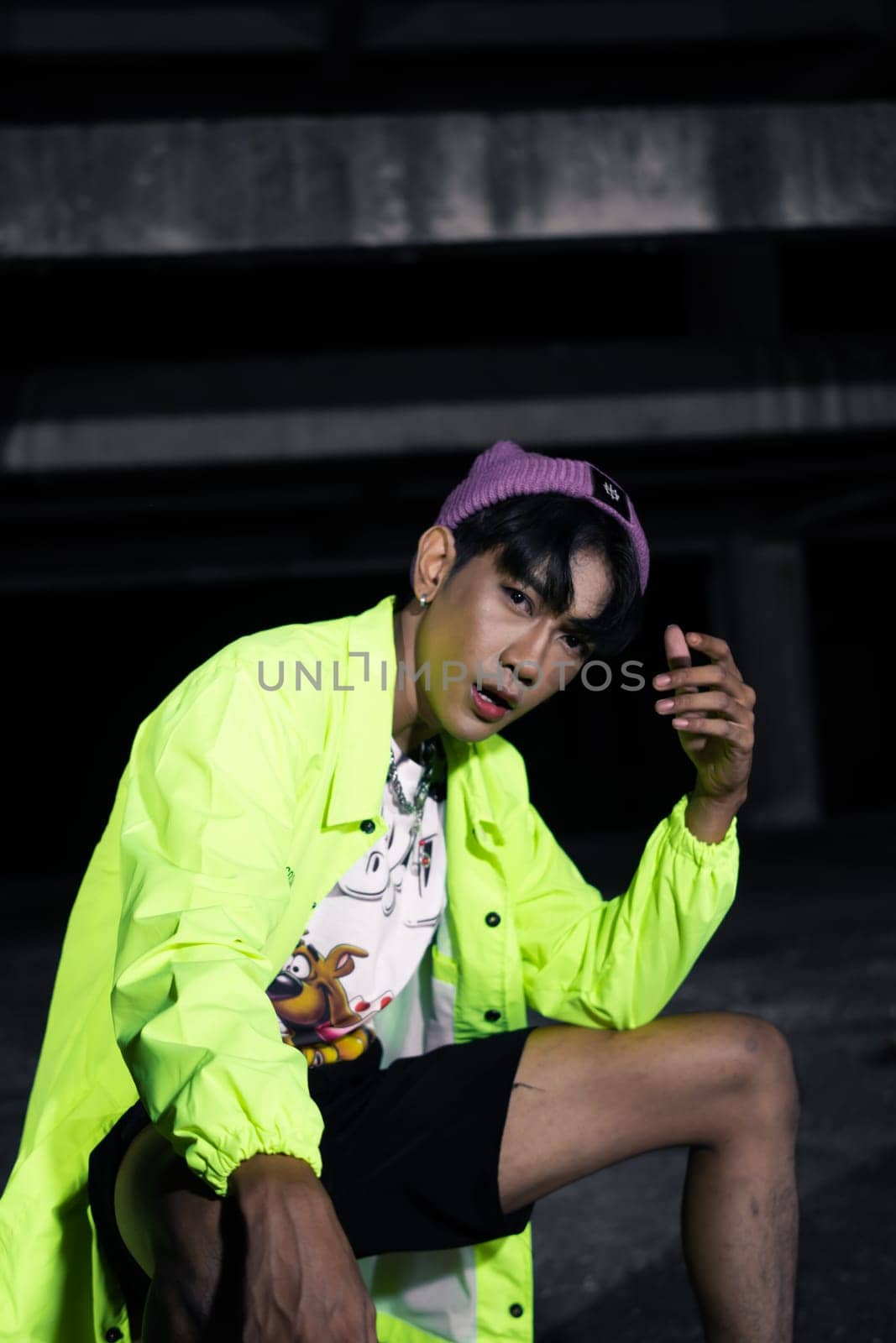an asian man in a green jacket posing and sitting very casually in an abandoned building