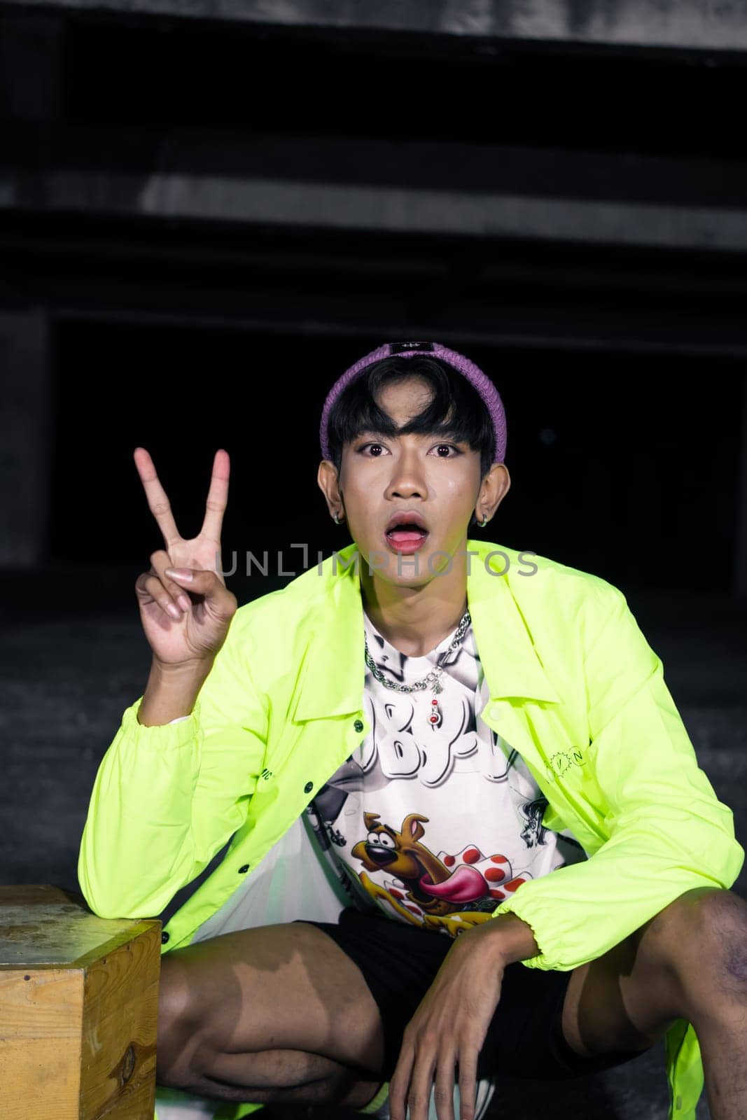 an asian man in a green jacket posing and sitting very casually in an abandoned building