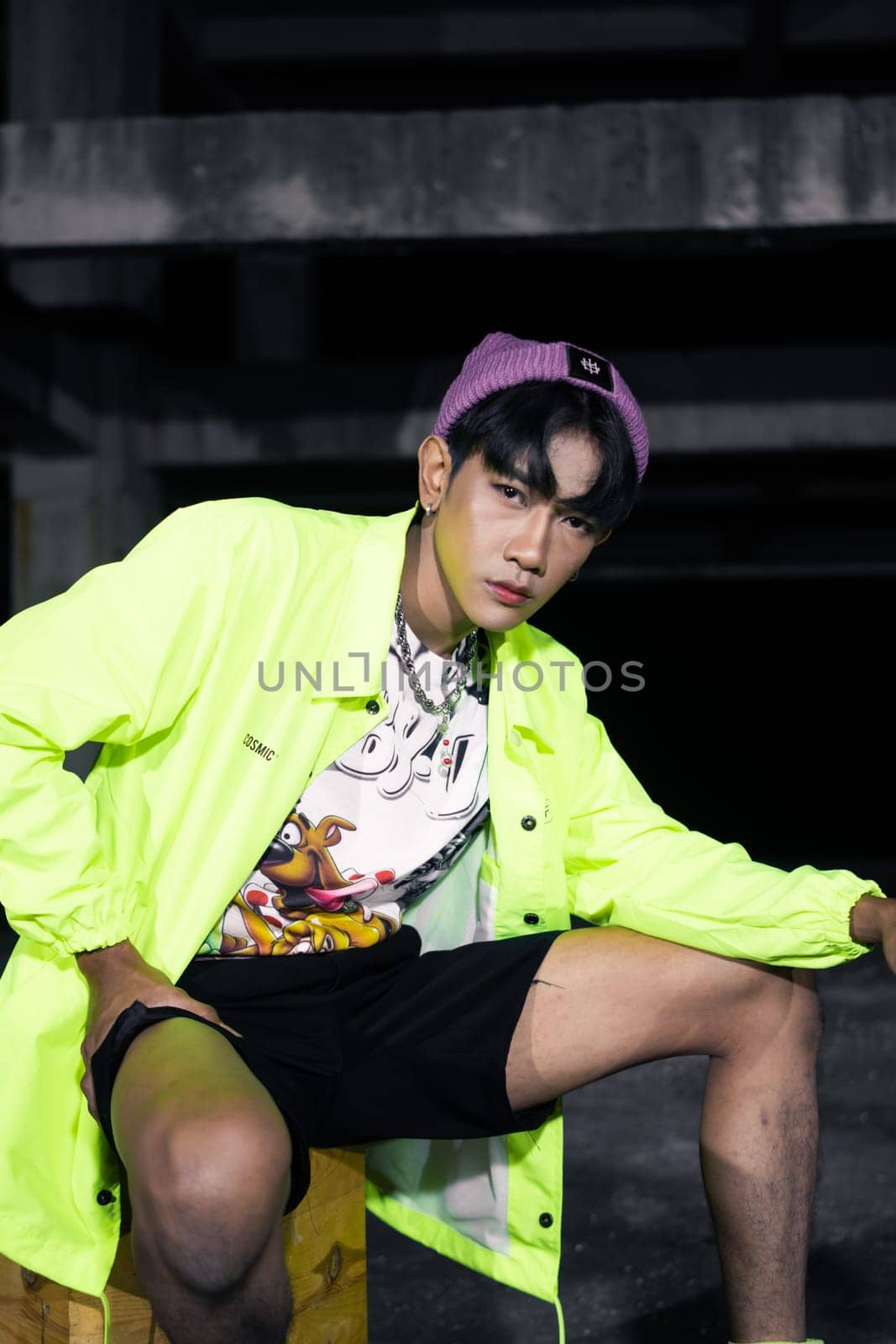 an asian man in a green jacket posing and sitting very casually in an abandoned building