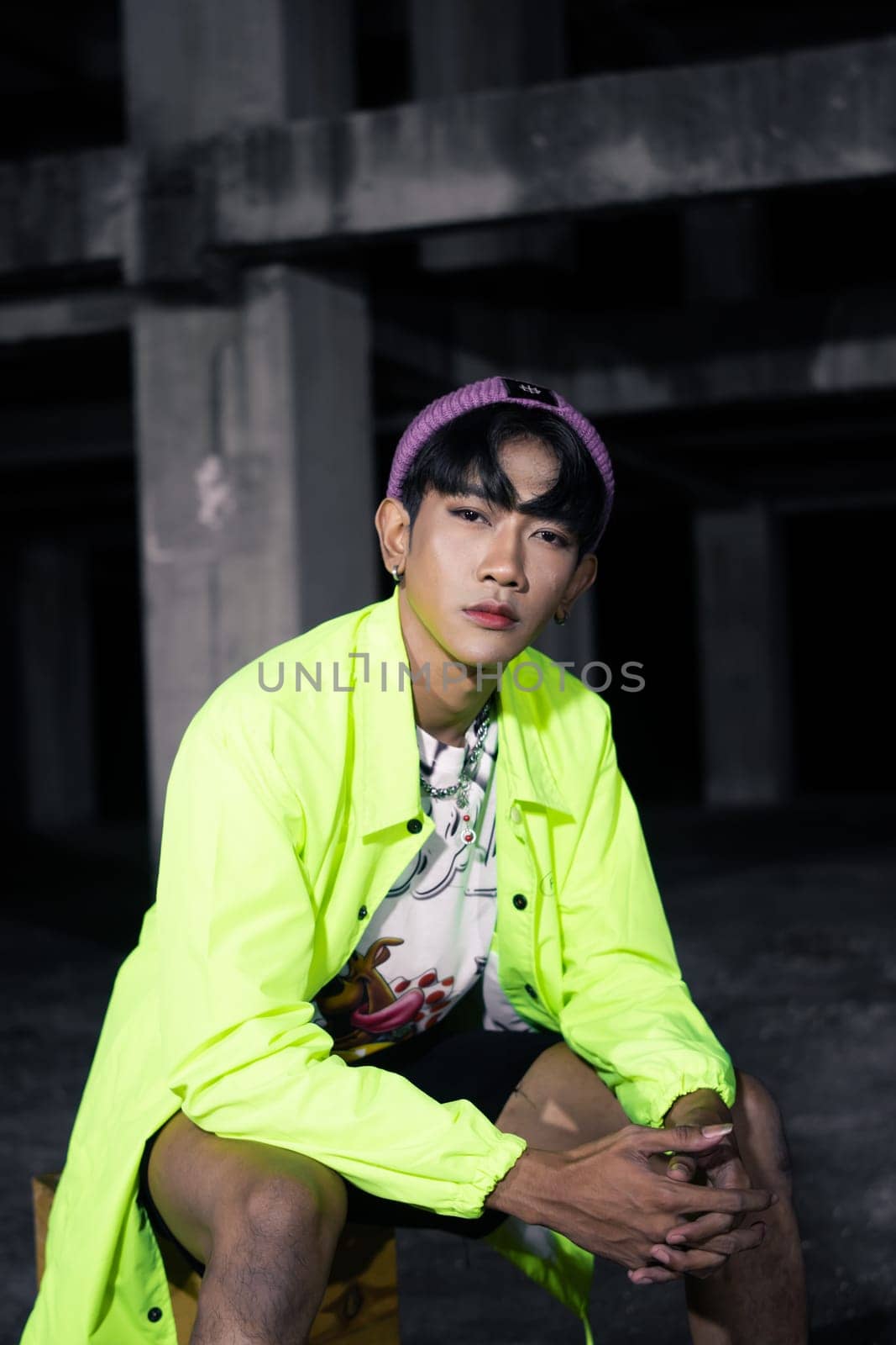 an asian man in a green jacket posing and sitting very casually in an abandoned building