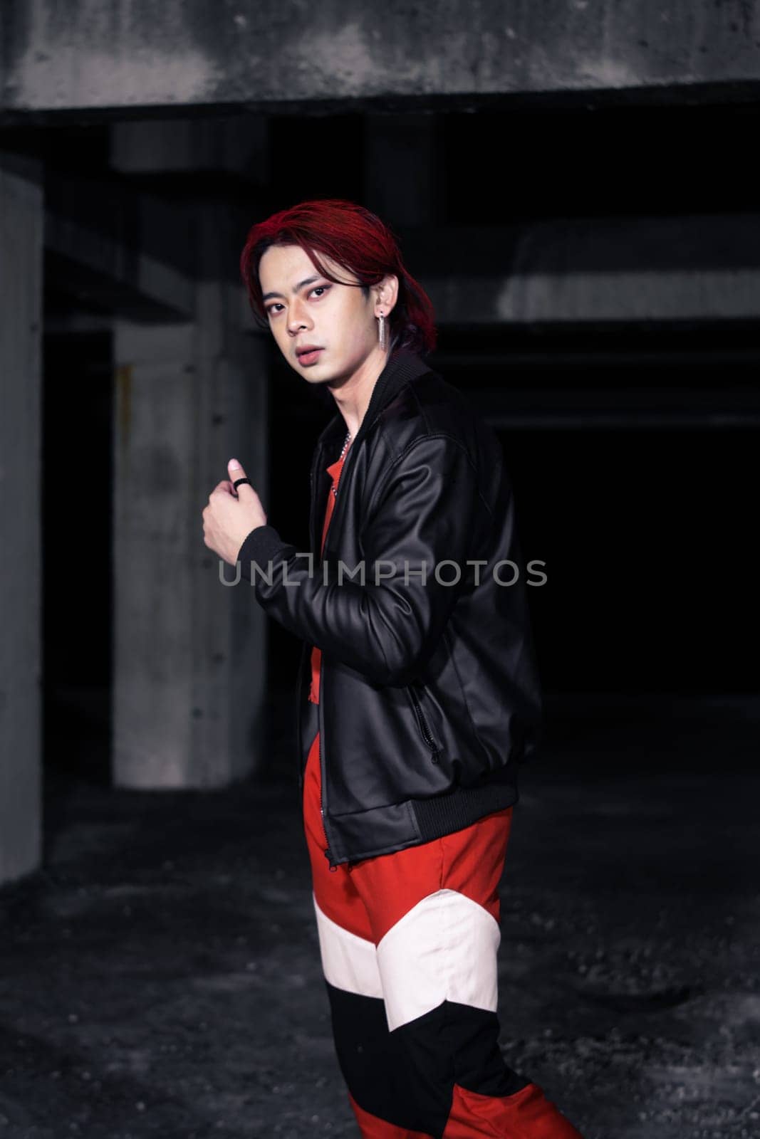 an asian man with red hair and a black jacket is posing in an abandoned building at night