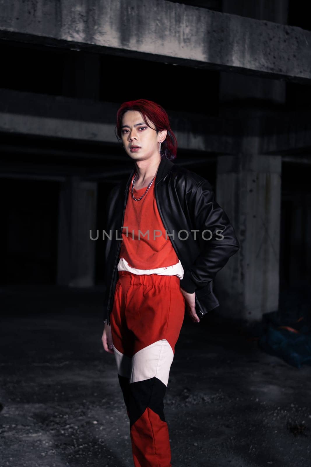 an asian man in a red shirt and earrings in his ears is standing in an abandoned building