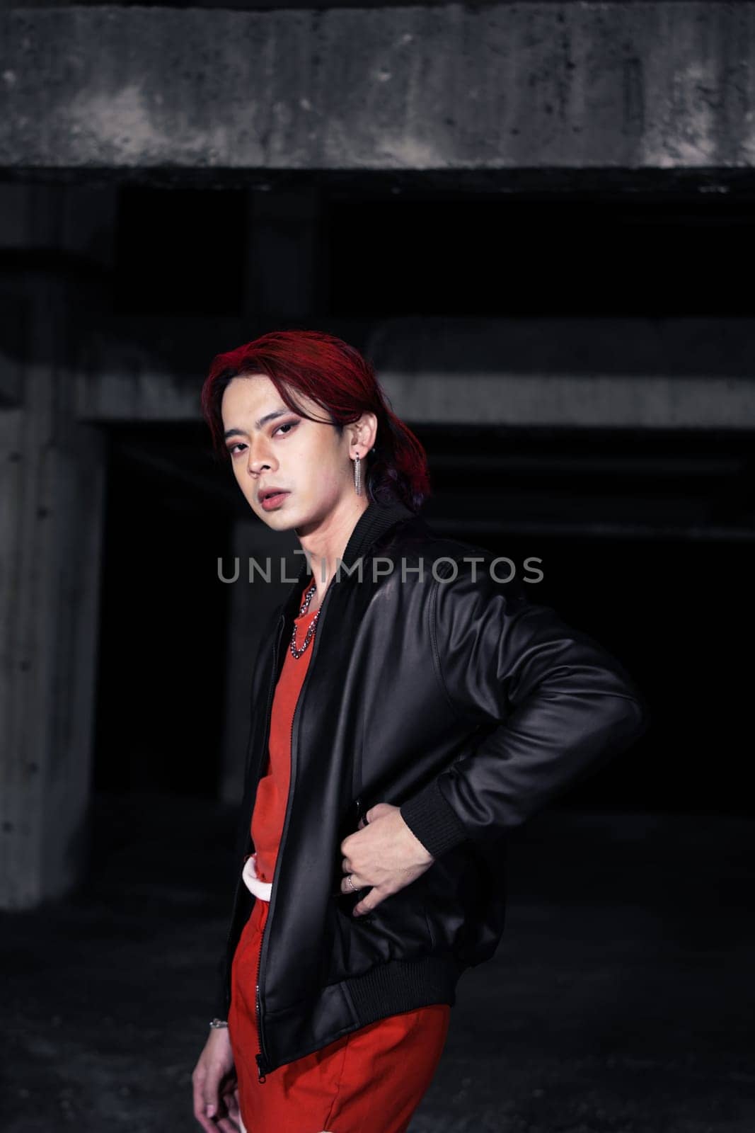 an asian man in a red shirt and earrings in his ears is standing in an abandoned building