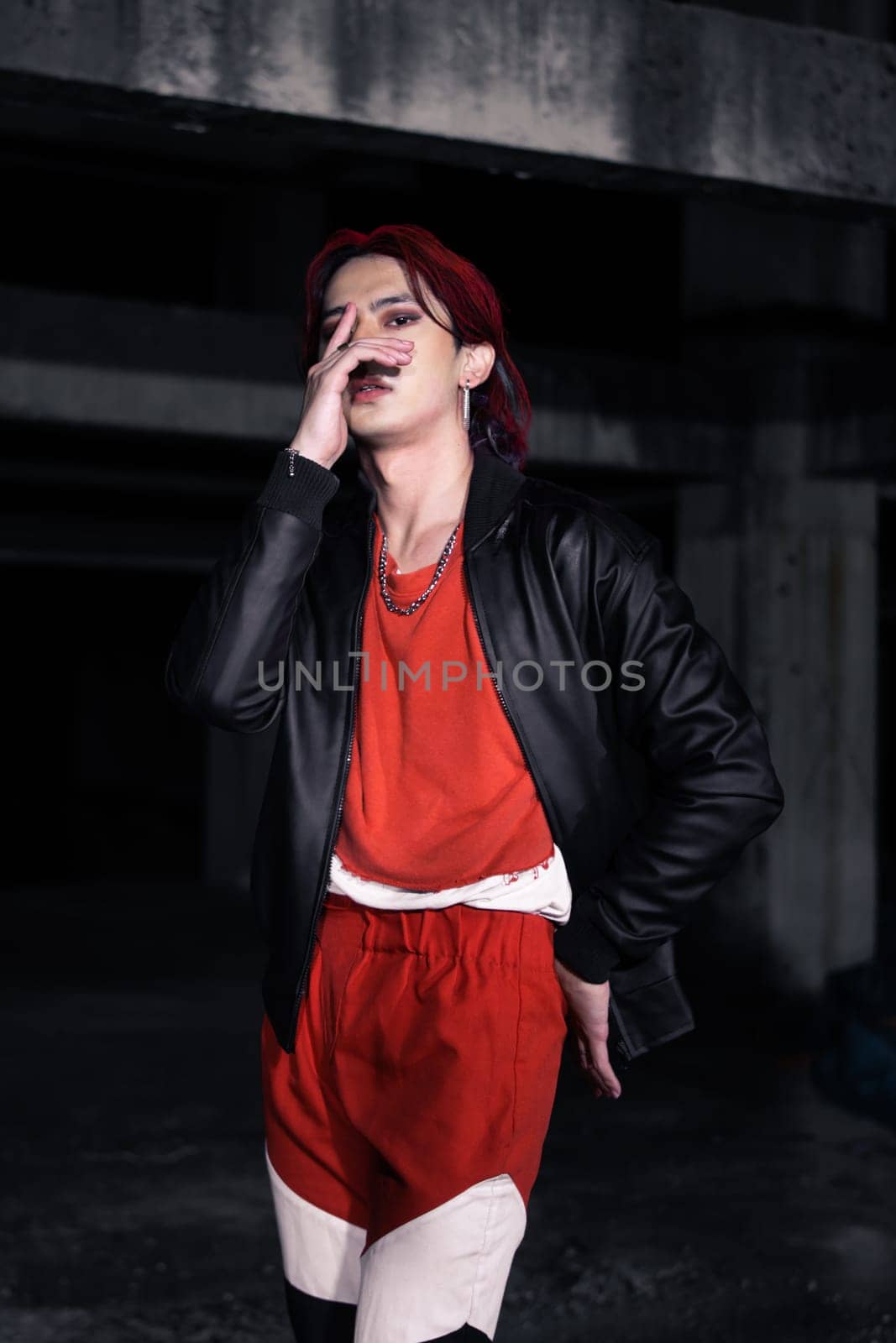 an asian man in a red shirt and earrings in his ears is standing in an abandoned building