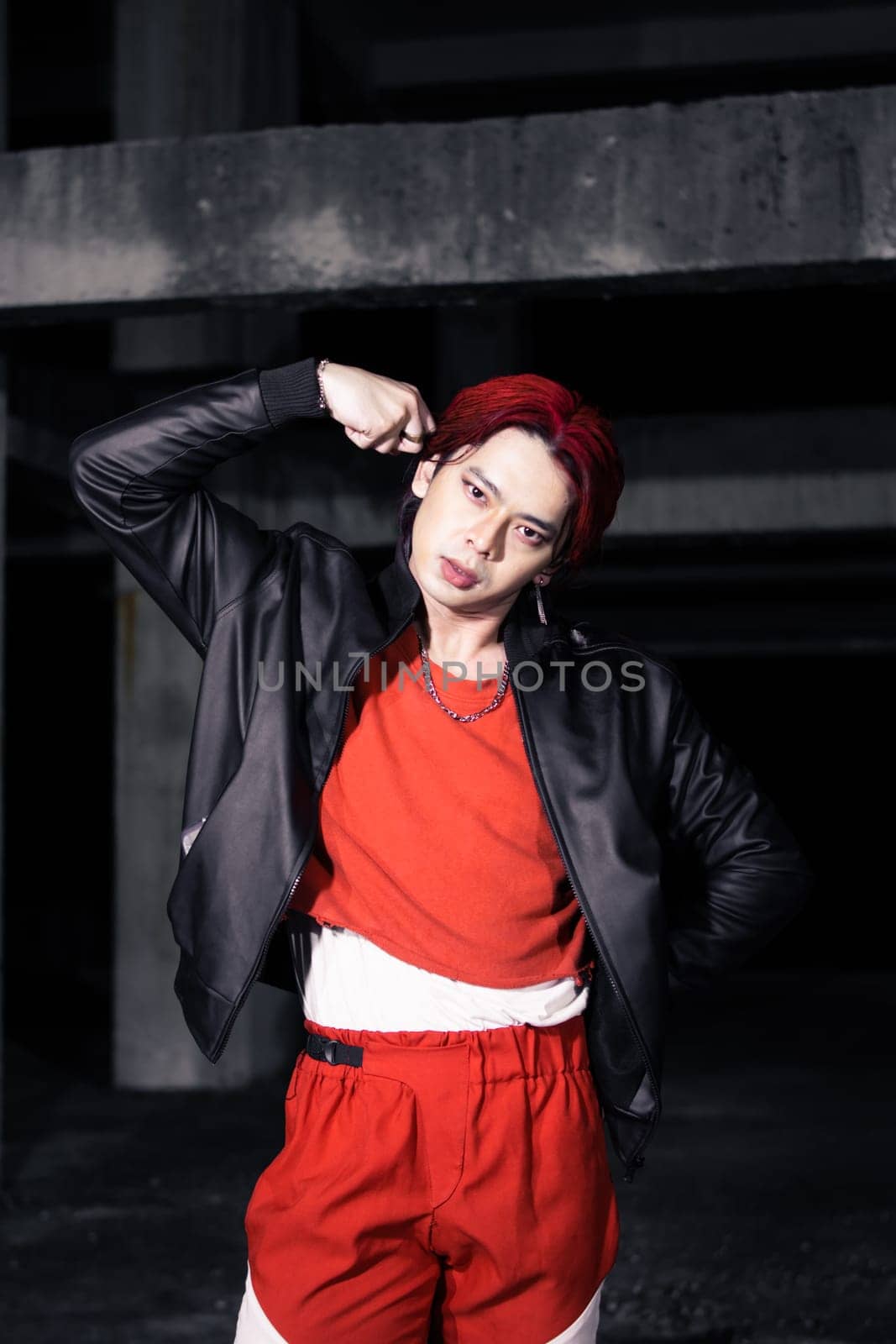 an asian man in a red shirt and black jacket posing with his hands in an abandoned warehouse