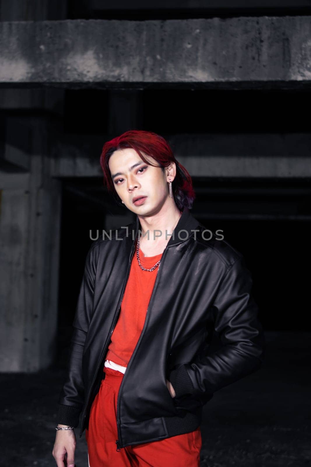 an asian man in a red shirt and earrings in his ears is standing in an abandoned building