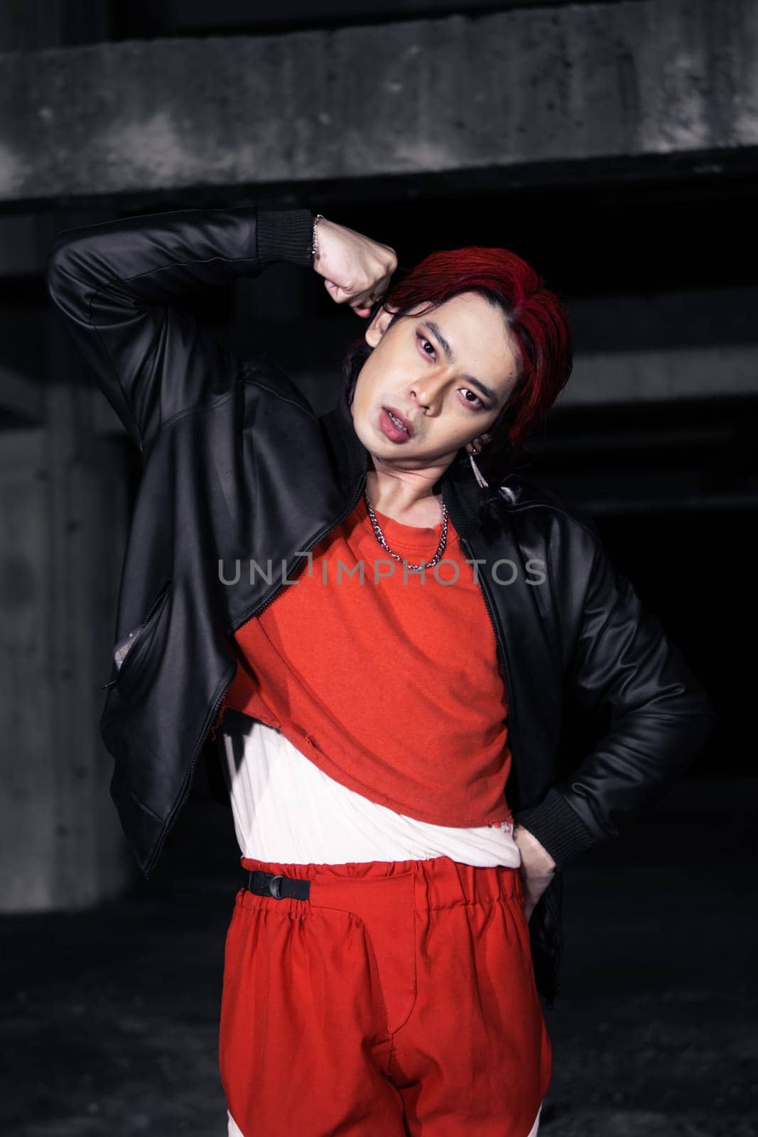 an asian man in a red shirt and black jacket posing with his hands in an abandoned warehouse