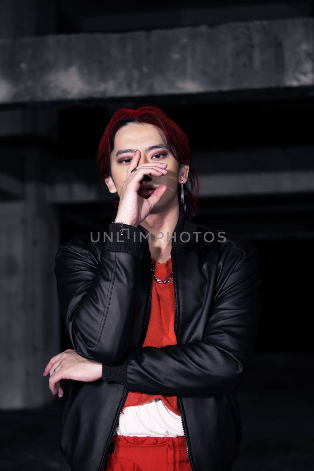 an asian man in a red shirt and black jacket posing with his hands in an abandoned warehouse