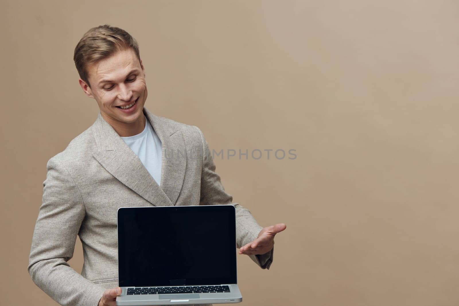 smiling young caucasian man hold laptop show blank screen wear casual jacket looking down isolated on beige background representing digital nomad lifestyle and cyberspace remote work concept