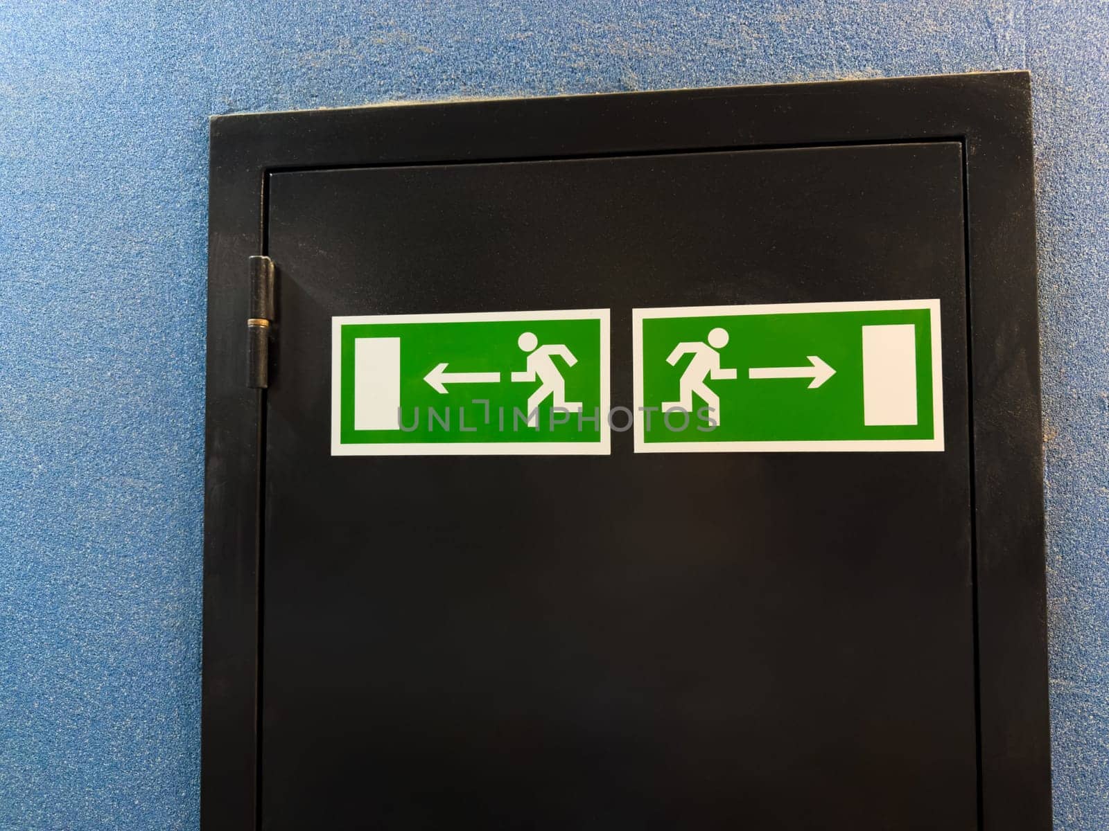 Universal exit signs with running figure and directional arrows illustrate internationally recognized emergency guidance system, offering nonverbal clarity across cultures in public buildings